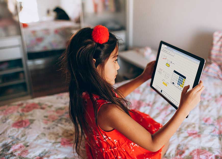 A young girl sitting on her bed using Modmath on a tablet.