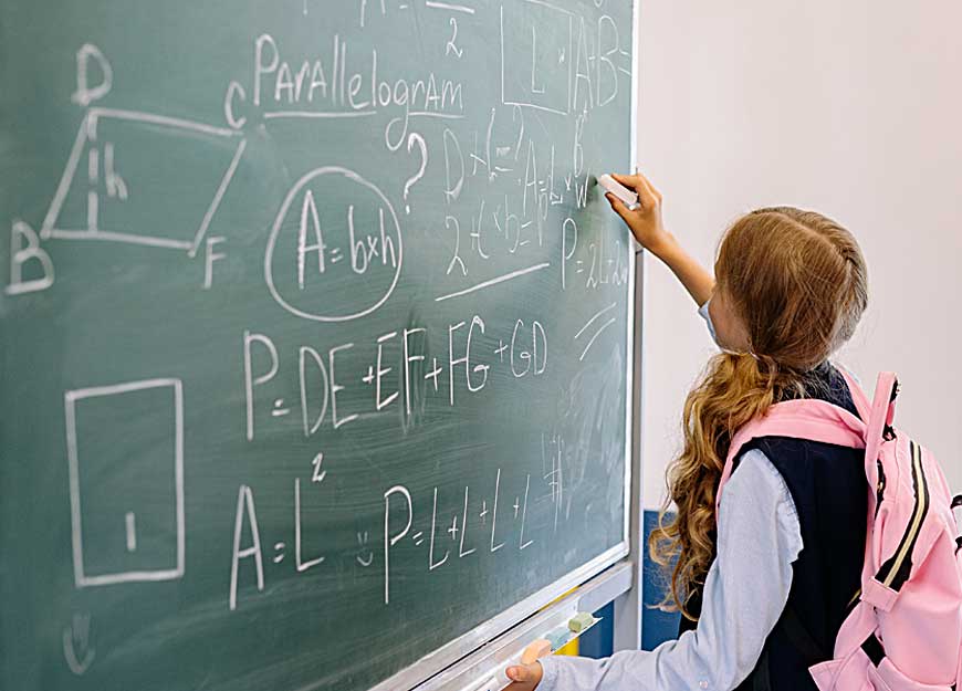 A student at a chalkboard writing out geometry area and perimeter formulas.